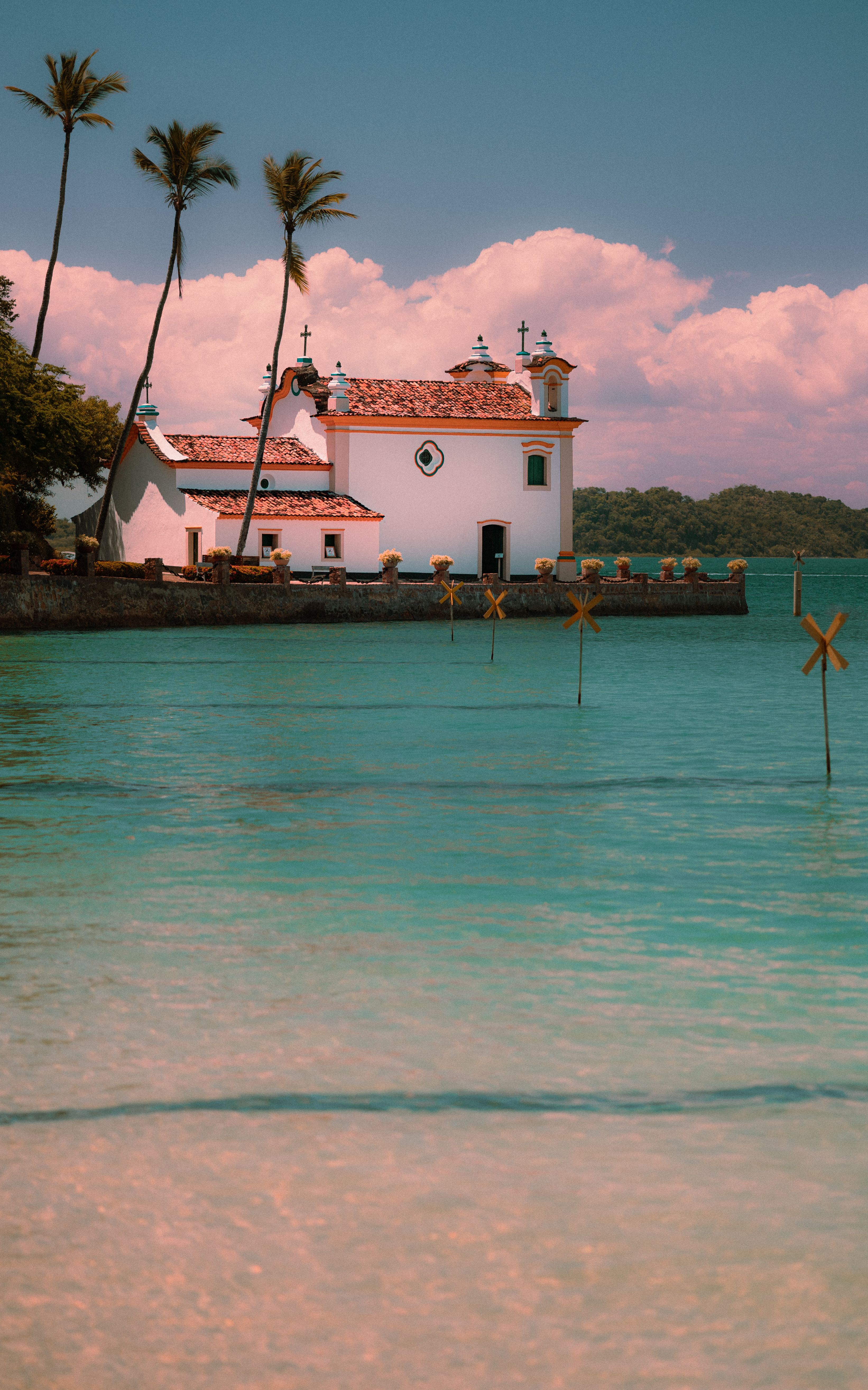 Idyllic tropical church on tranquil waters with palm trees under a clear sky.