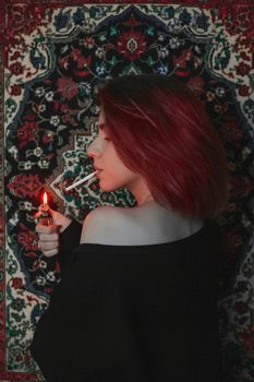 Moody portrait of a woman with red hair lighting a cigarette against a vibrant patterned backdrop.