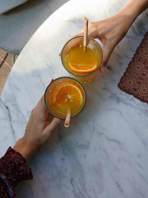 Two hands holding glasses of orange juice on a marble table, top view.