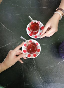 Two cups of Turkish tea on a dark marble table viewed from above, featuring decorative saucers.