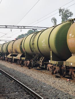 A freight train with green fuel tankers parked on railway tracks under clear skies.