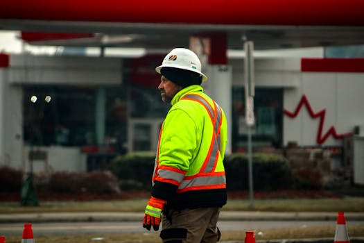 A construction worker wearing high-visibility gear and a helmet at a roadside in Canada.