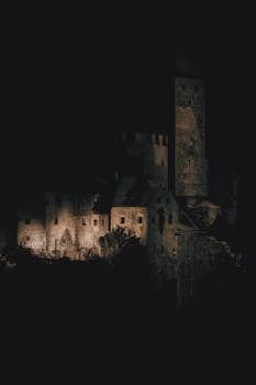 A dramatic nighttime view of a medieval castle illuminated against darkness, exuding mystery.