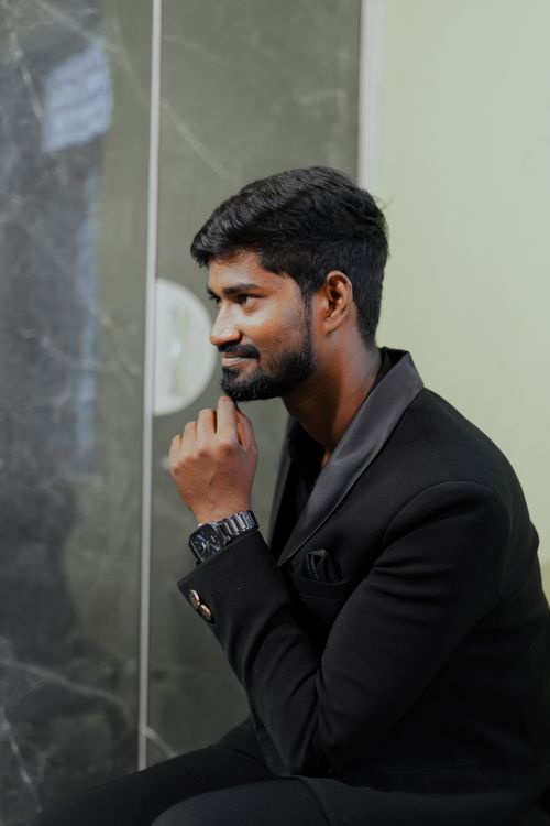 Free Thoughtful man in black suit sits indoors, wearing a stylish watch. Stock Photo