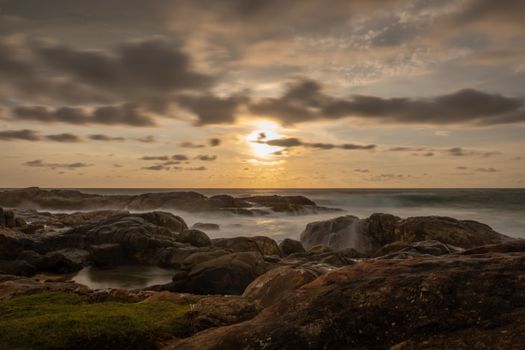 Dramatic sunset over the rocky coast of Sri Lanka with ocean waves crashing against the shore.