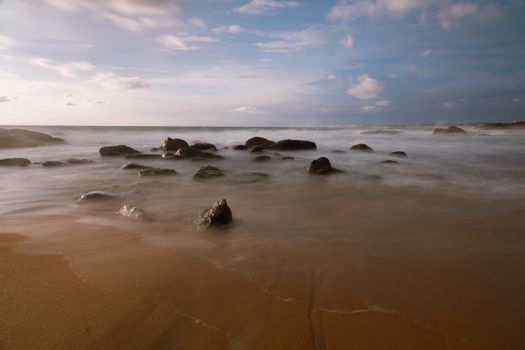 Tranquil beach scene with rocks and ocean waves at sunset in Sri Lanka.