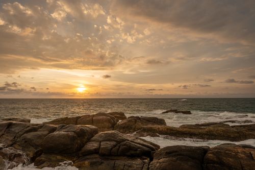 Free Serene view of a sunset illuminating a rocky beach and ocean waves in Sri Lanka. Stock Photo