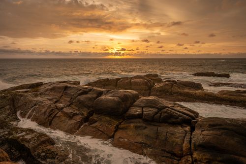 Free Stunning rocky shoreline and ocean waves under a vibrant sunset sky. Stock Photo