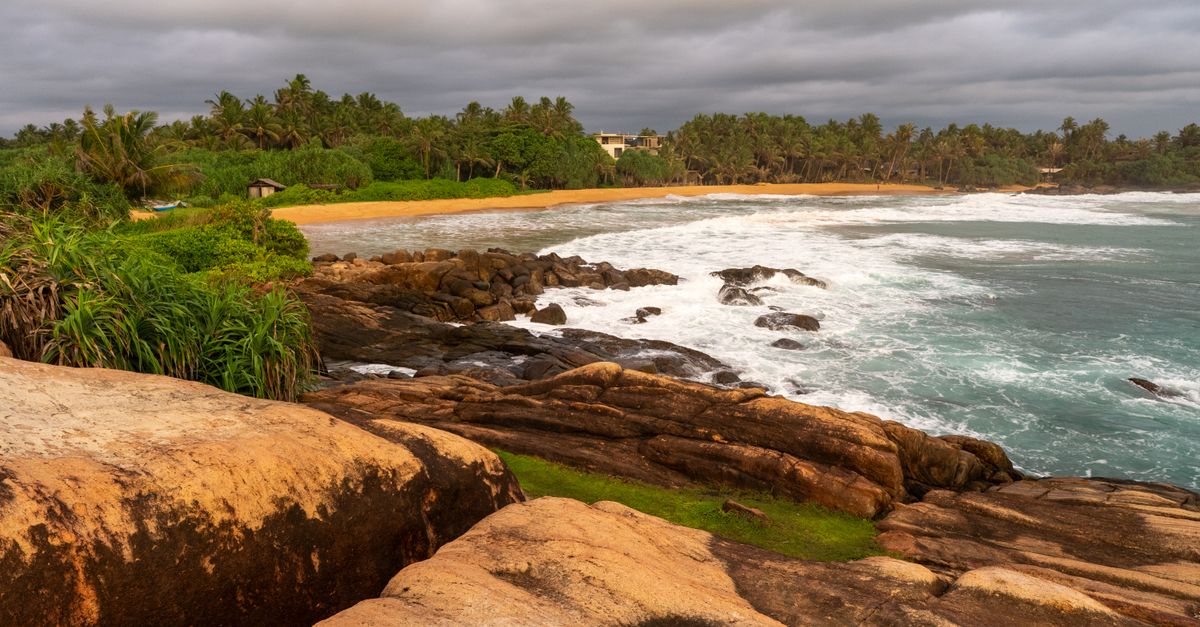 A rocky Sri Lankan shoreline at sunset with the sea breaking on it
