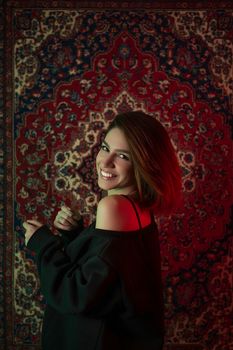 A young woman smiles warmly against a detailed, colorful tapestry background.