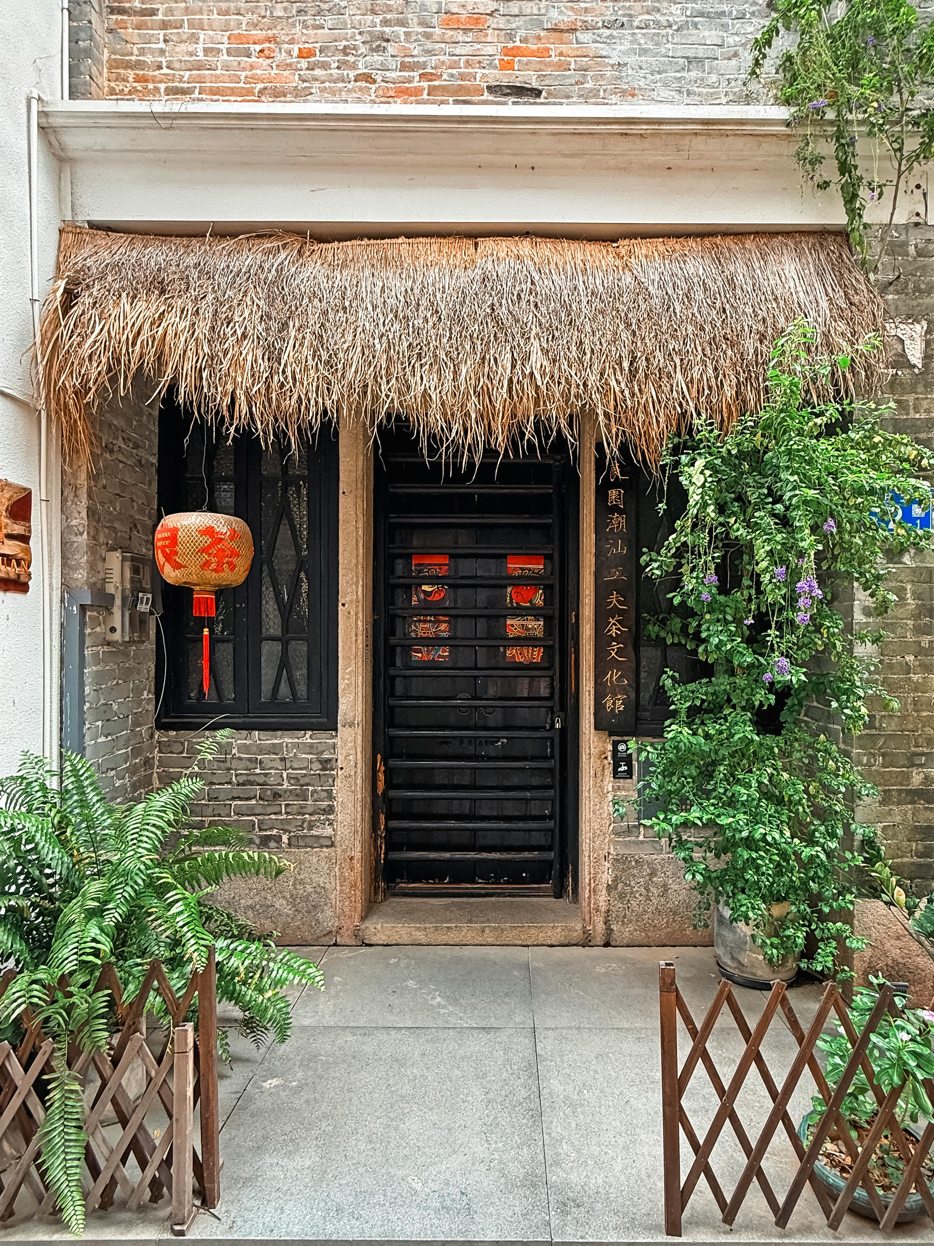 A rustic Chinese doorway with a straw roof and red lanterns, showcasing traditional architecture.