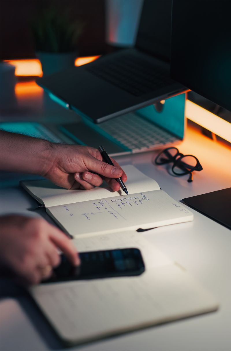 Hands writing notes on a desk with a laptop nearby
