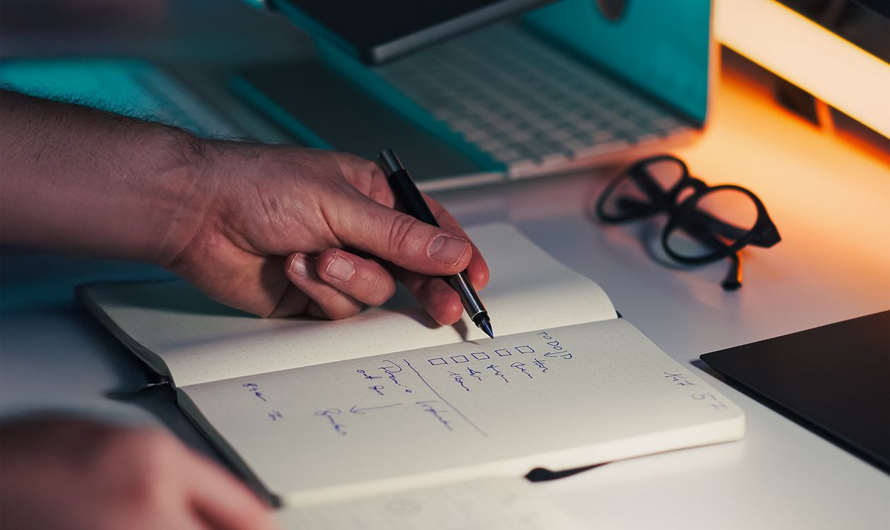Hands making notes beside a laptop, illustrating a project evidence review