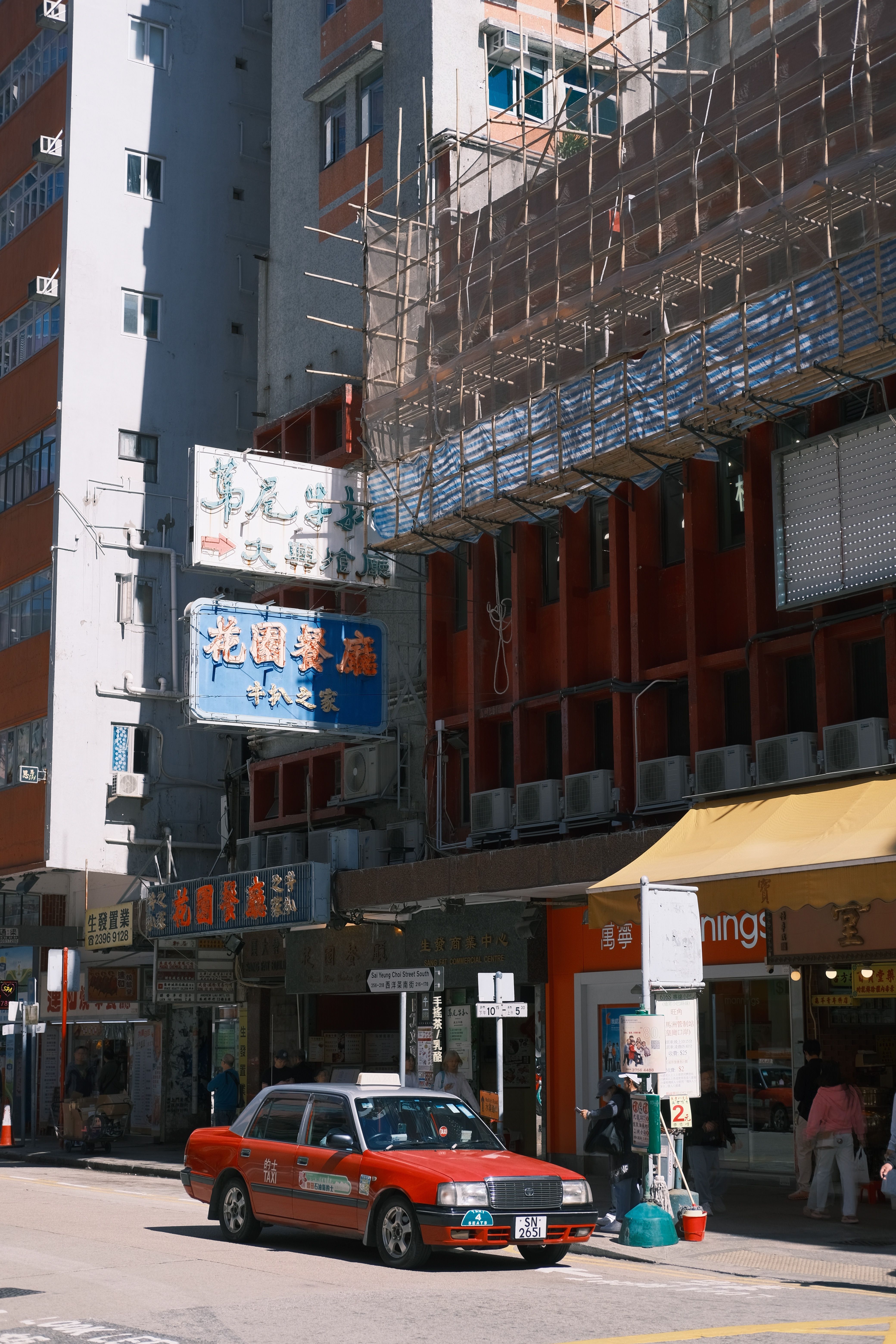무료 붉은 택시와 전통적인 비계가 있는 홍콩의 거리 풍경이 현대적인 건물과 대조를 이룹니다. 스톡 사진
