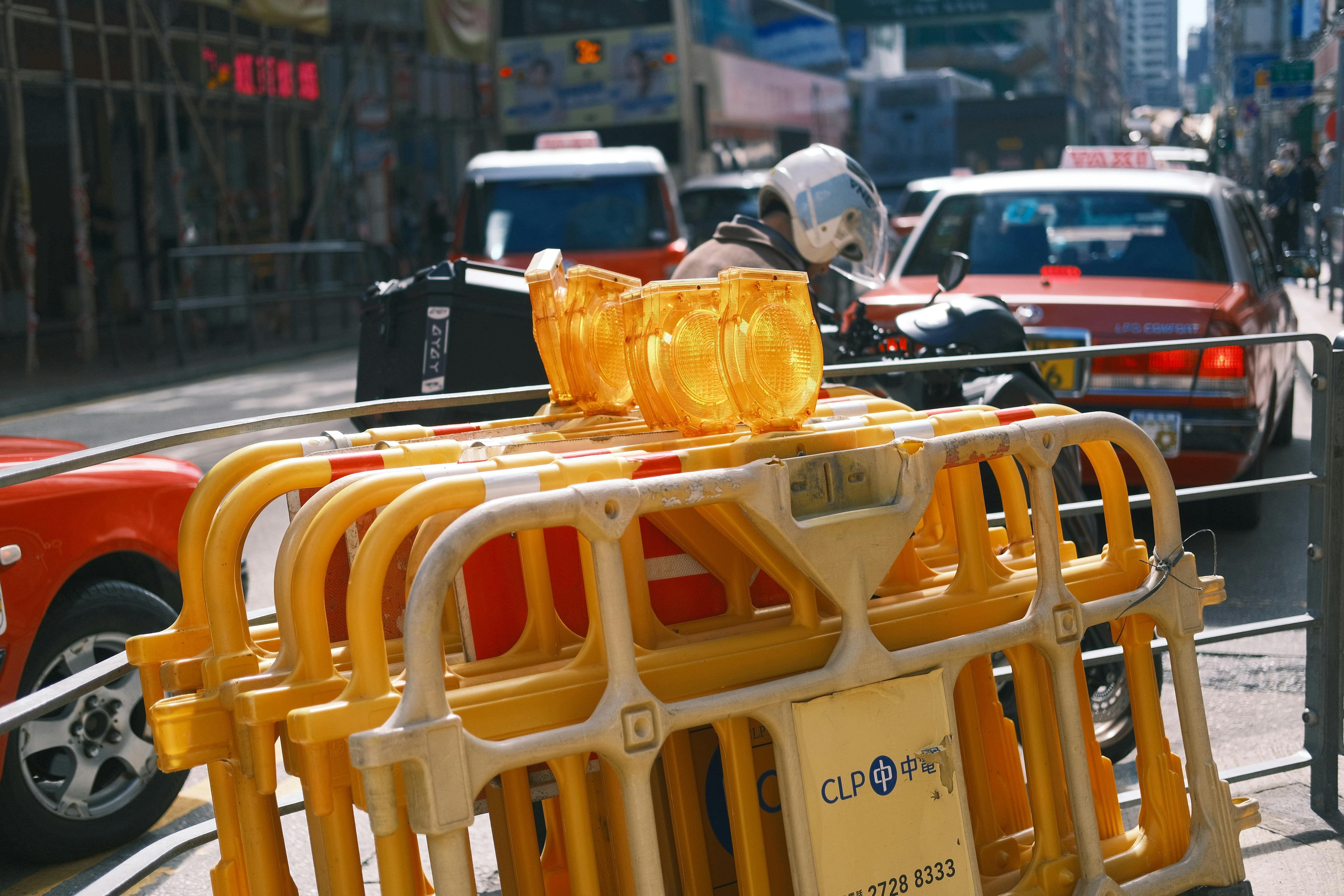 A busy urban street with traffic barriers and taxis on a sunny day.