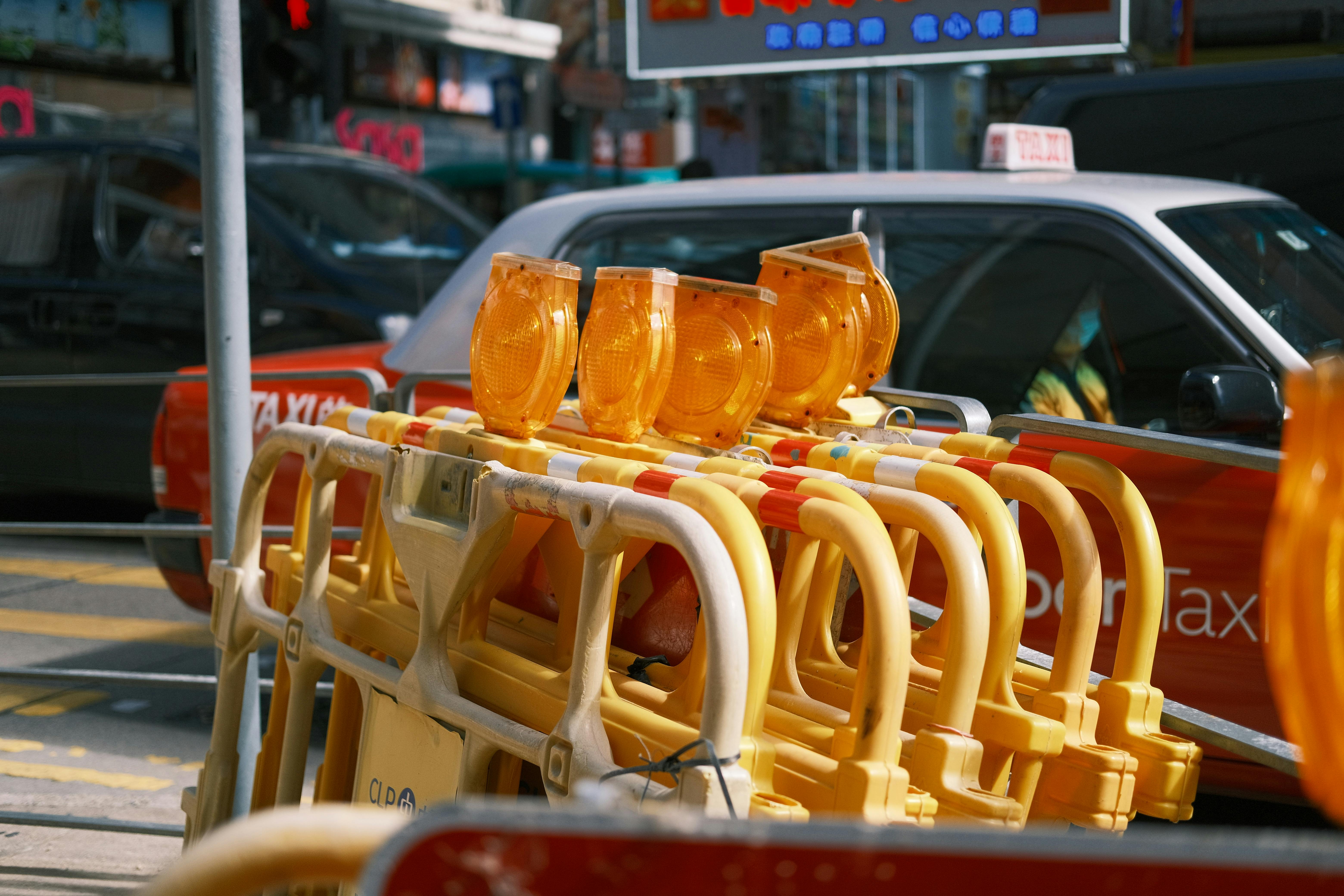 Traffic barriers with yellow lights in a city street with taxis in the background.