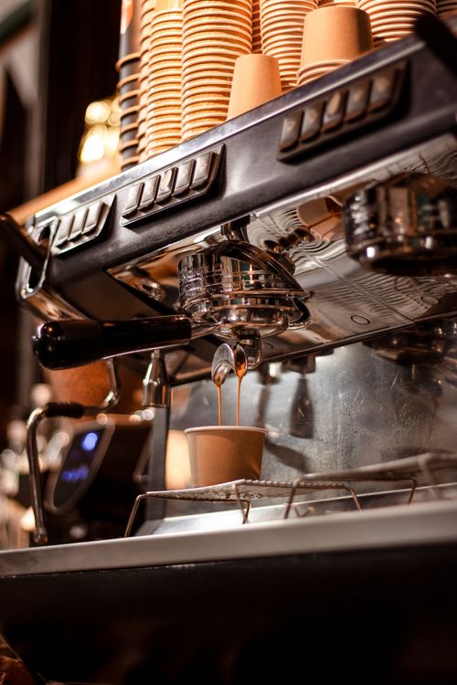 Free Espresso machine brewing fresh coffee into takeaway cup with warm lighting. Stock Photo