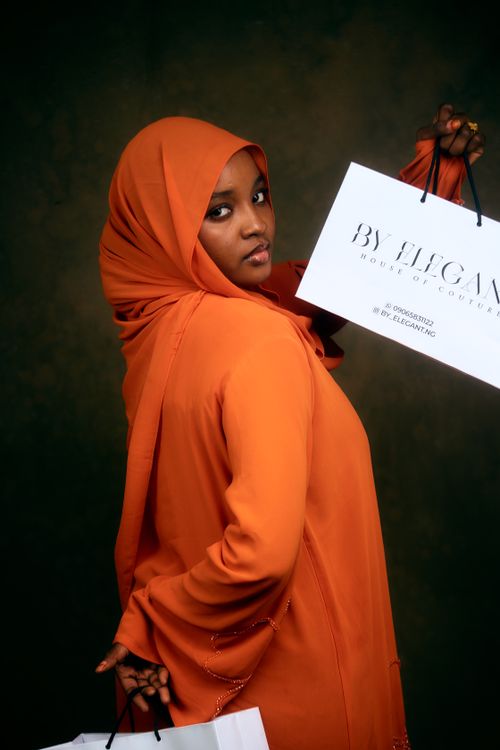Free Elegant woman in orange hijab holding a shopping bag, showcasing fashionable attire. Ideal for lifestyle and fashion themes. Stock Photo