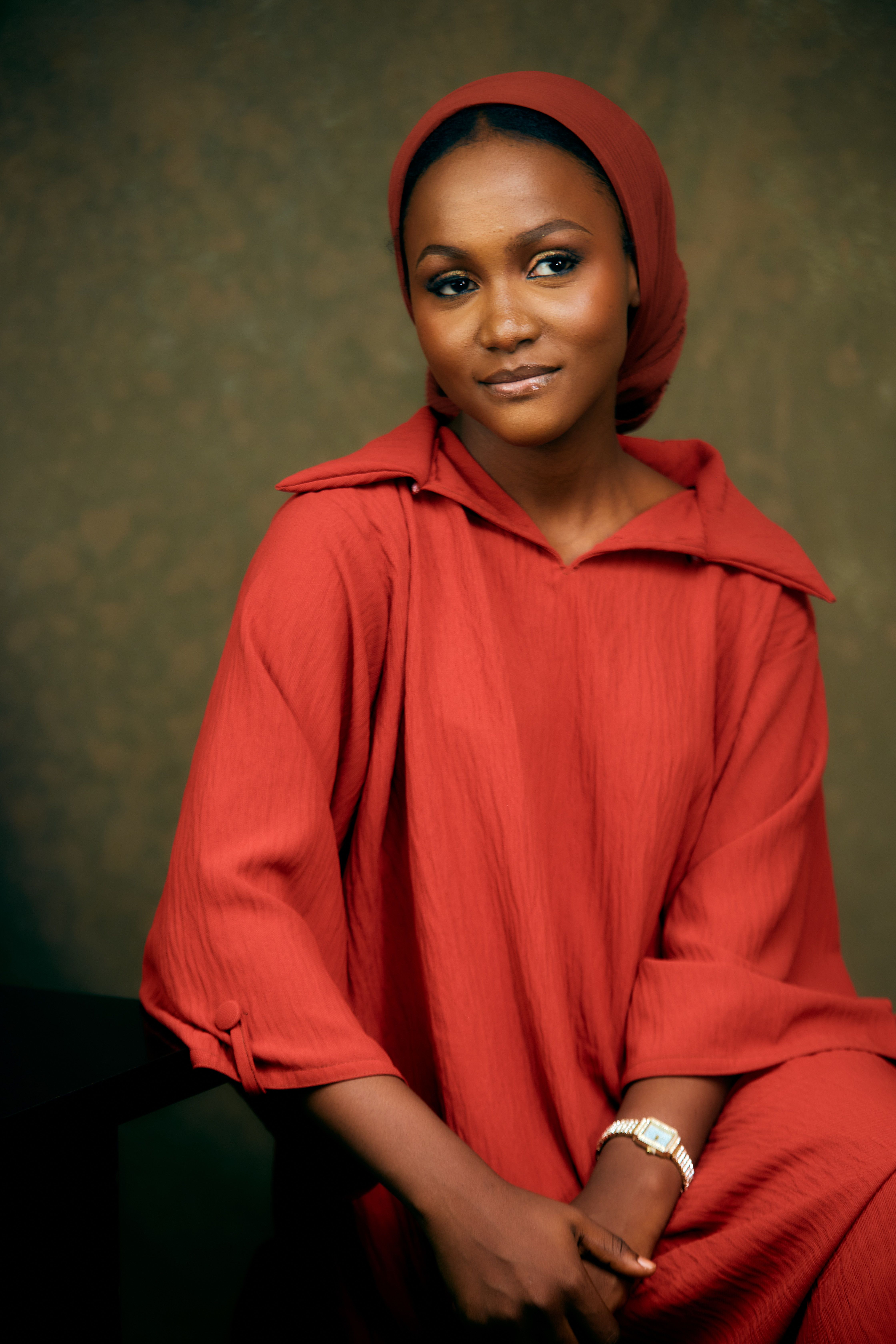 Portrait of an elegant woman wearing a red dress and headscarf, looking pensive.