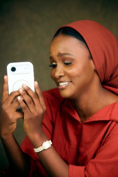Cheerful woman in red headscarf taking a selfie with her smartphone indoors.