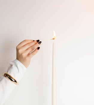 A woman's hand elegantly lighting a tall white candle with a match.