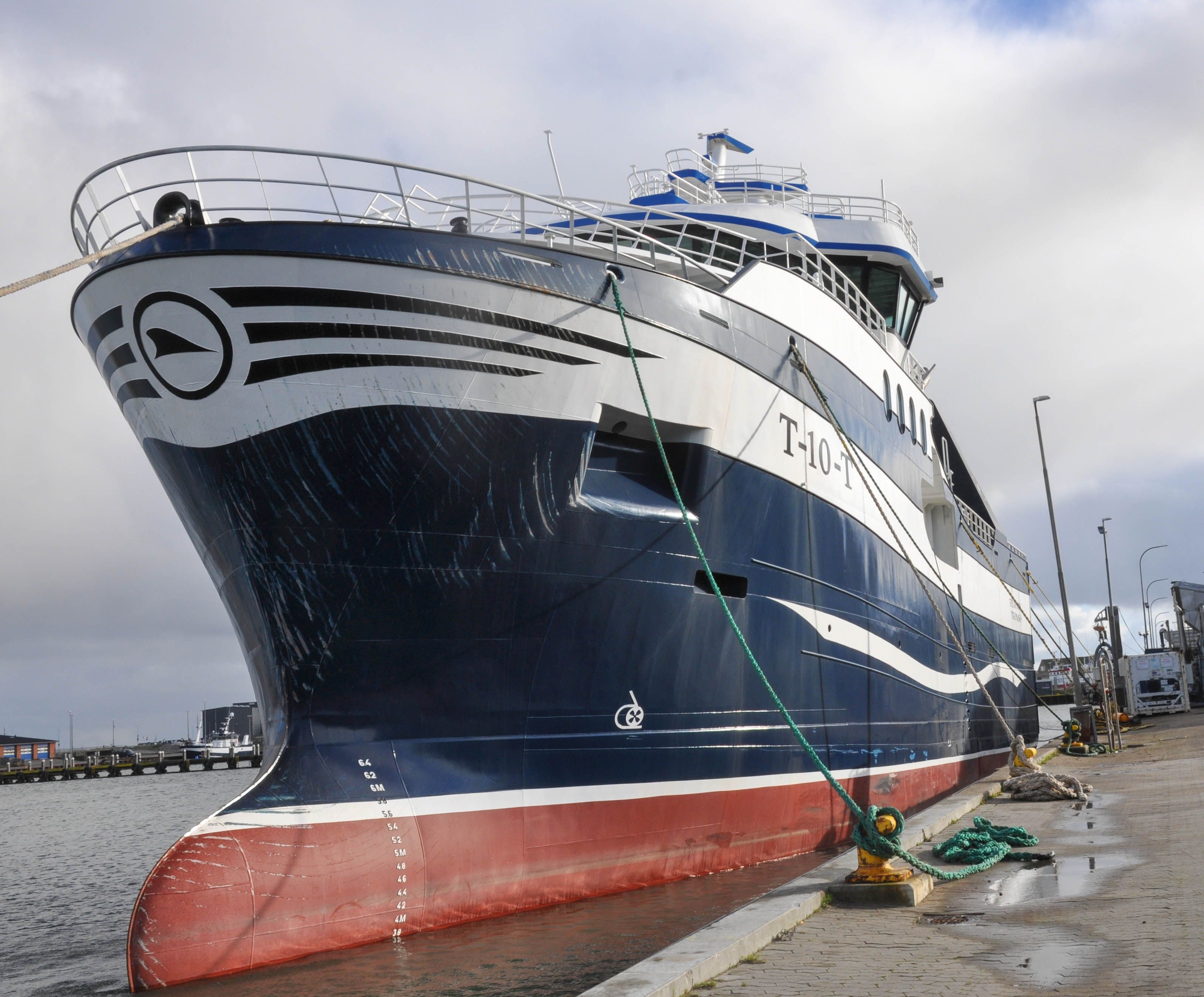 Large fishing vessel docked at Hvide Sande harbor, Denmark, under cloudy skies.