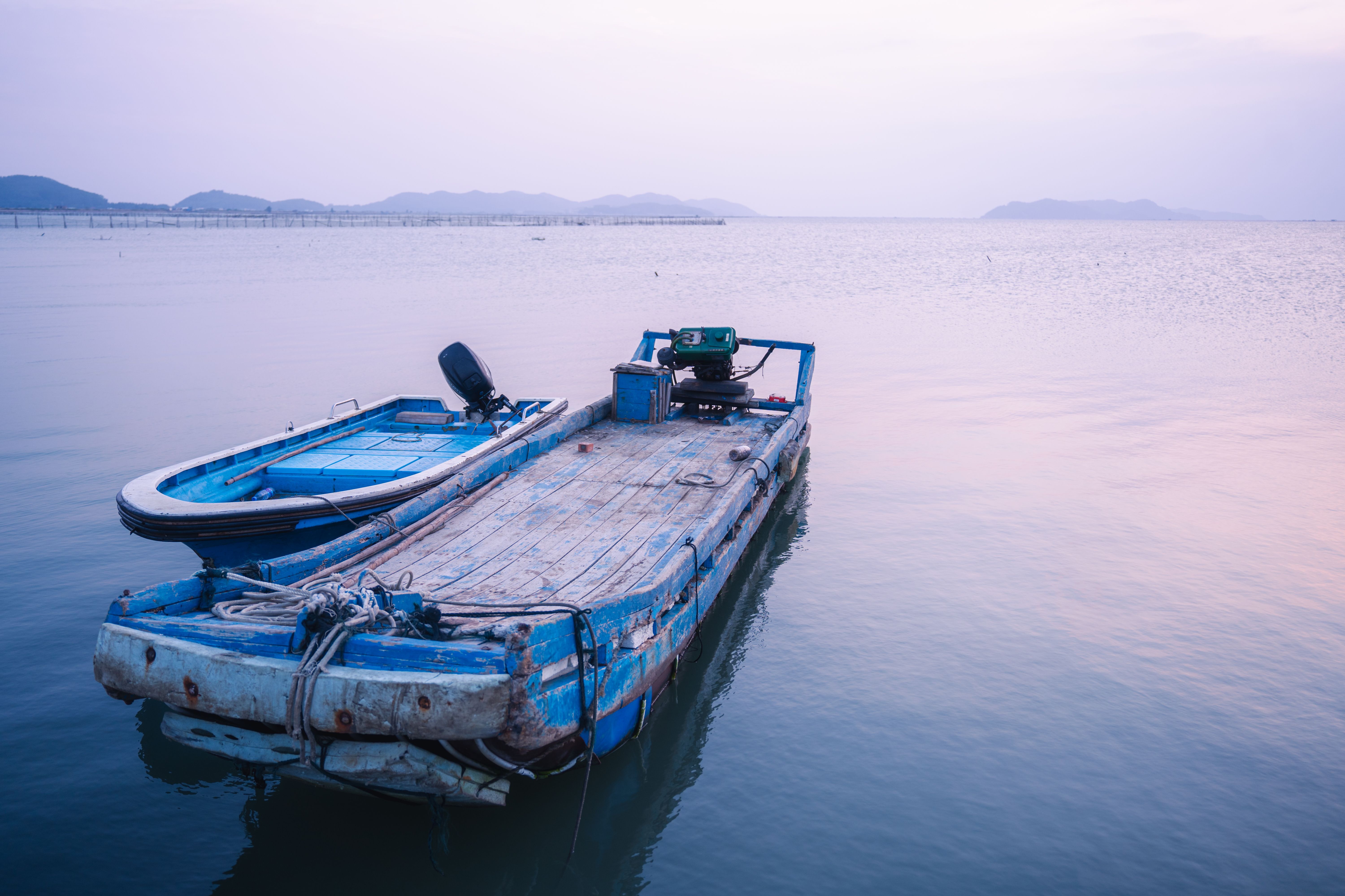 Two blue boats anchored on calm sea reflecting an evening sky, creating a tranquil and peaceful scene.