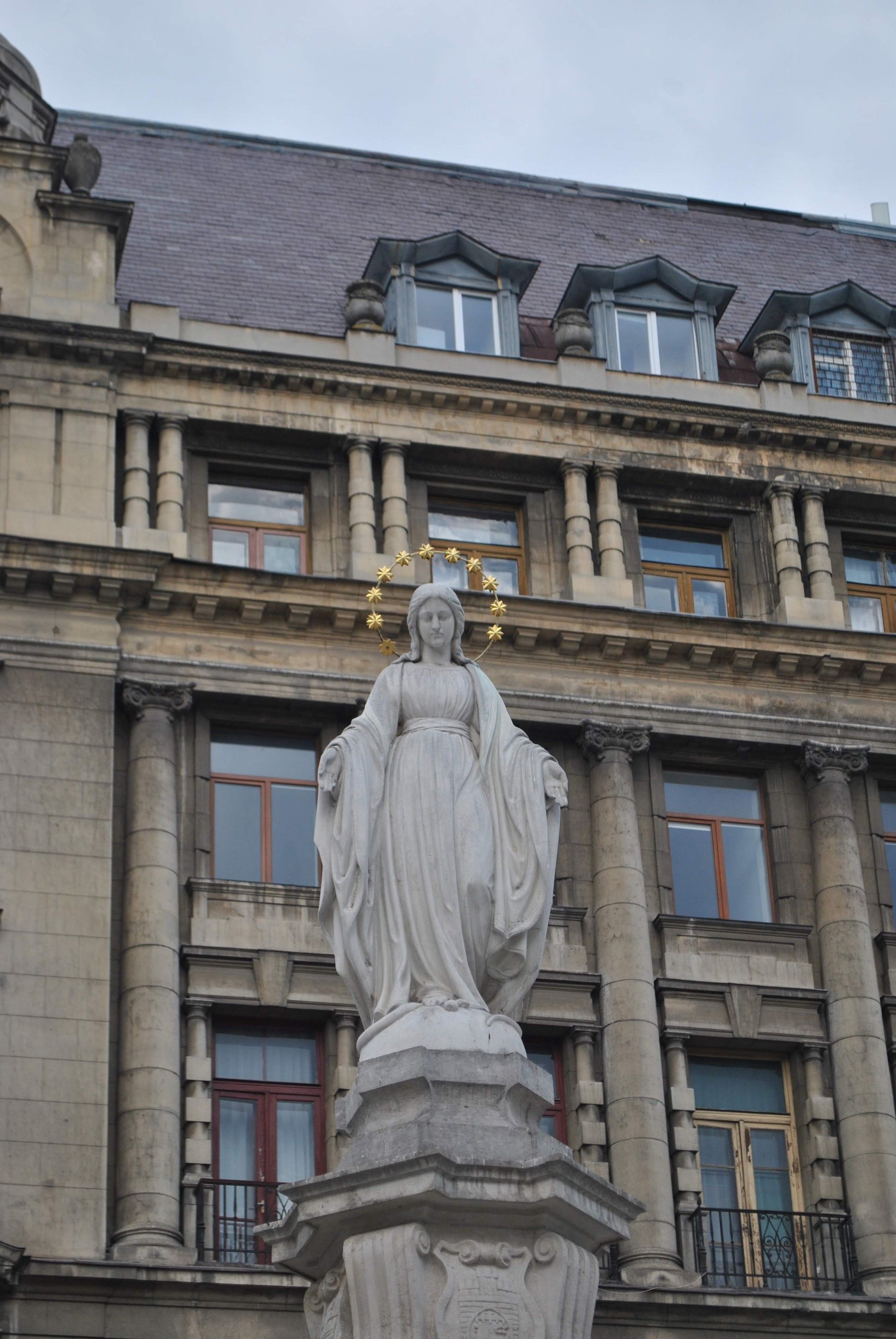 A grand statue of the Madonna with a crown backdrop stands against a historic building facade.