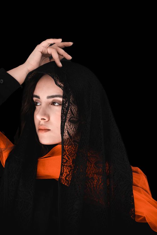 Free Striking portrait of a woman in black lace and orange scarf, against black background. Stock Photo