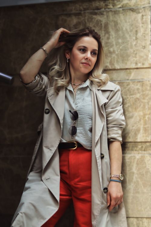Free Fashionable woman posing indoors wearing a trench coat and red pants. Stock Photo