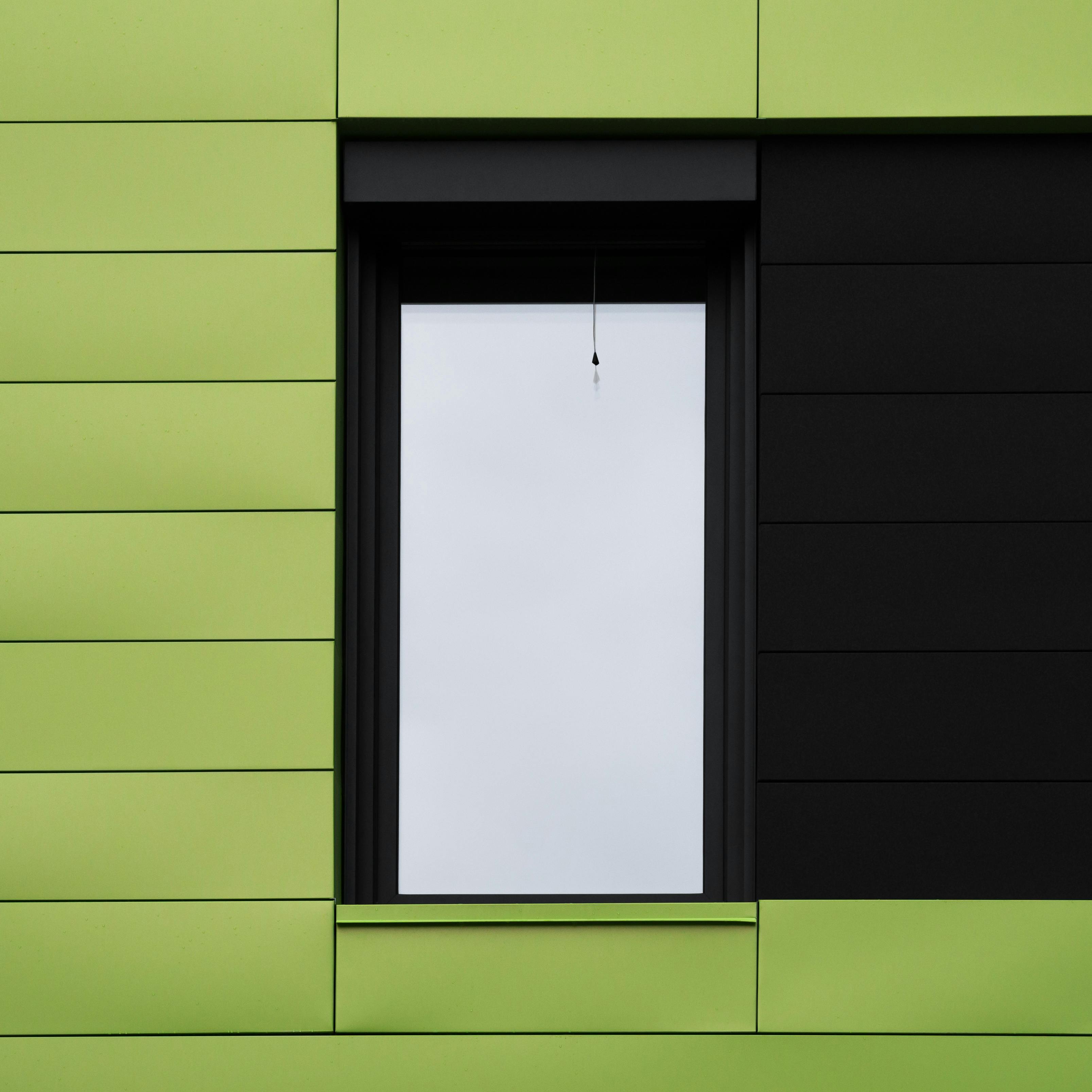 Abstract view of a modern building facade with green and black panels and a single window.