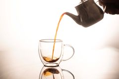 Elegant tea being poured from teapot into glass cup, with reflection.
