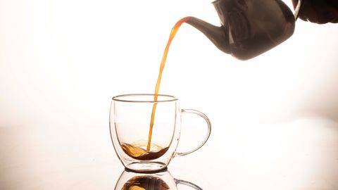 Elegant tea being poured from teapot into glass cup, with reflection.