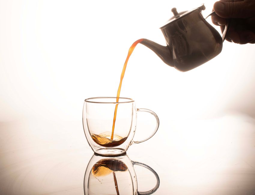 Elegant tea being poured from teapot into glass cup, with reflection.