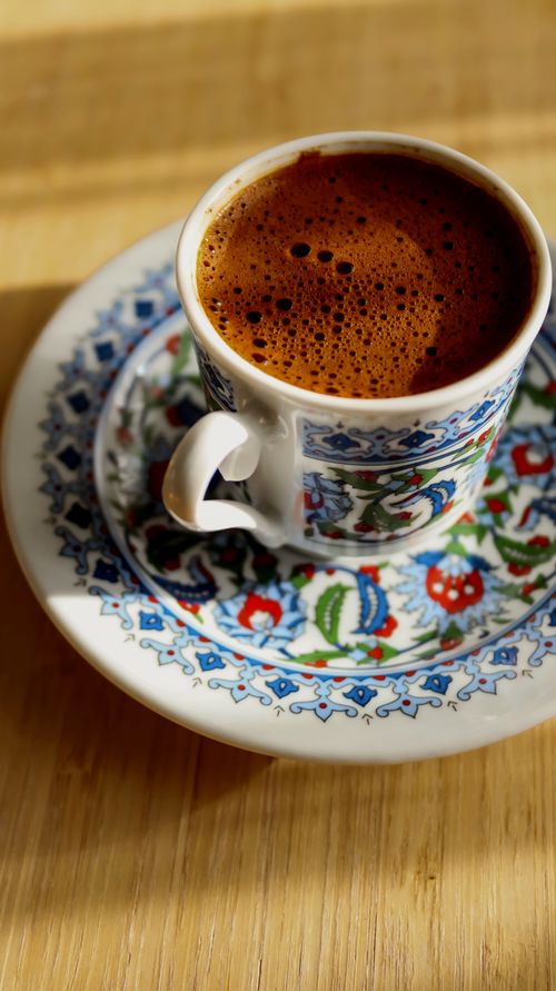 Free A steaming cup of Turkish coffee in an intricately designed cup set on a wooden table. Stock Photo