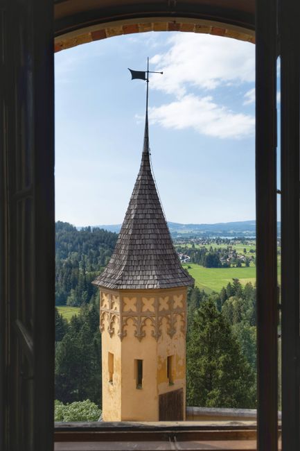 A picturesque view of a medieval castle tower framed by a window, overlooking lush green landscape.