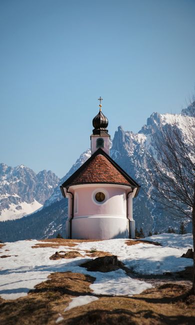 Serene chapel amidst snowy mountains under a clear blue sky, capturing winter tranquility.