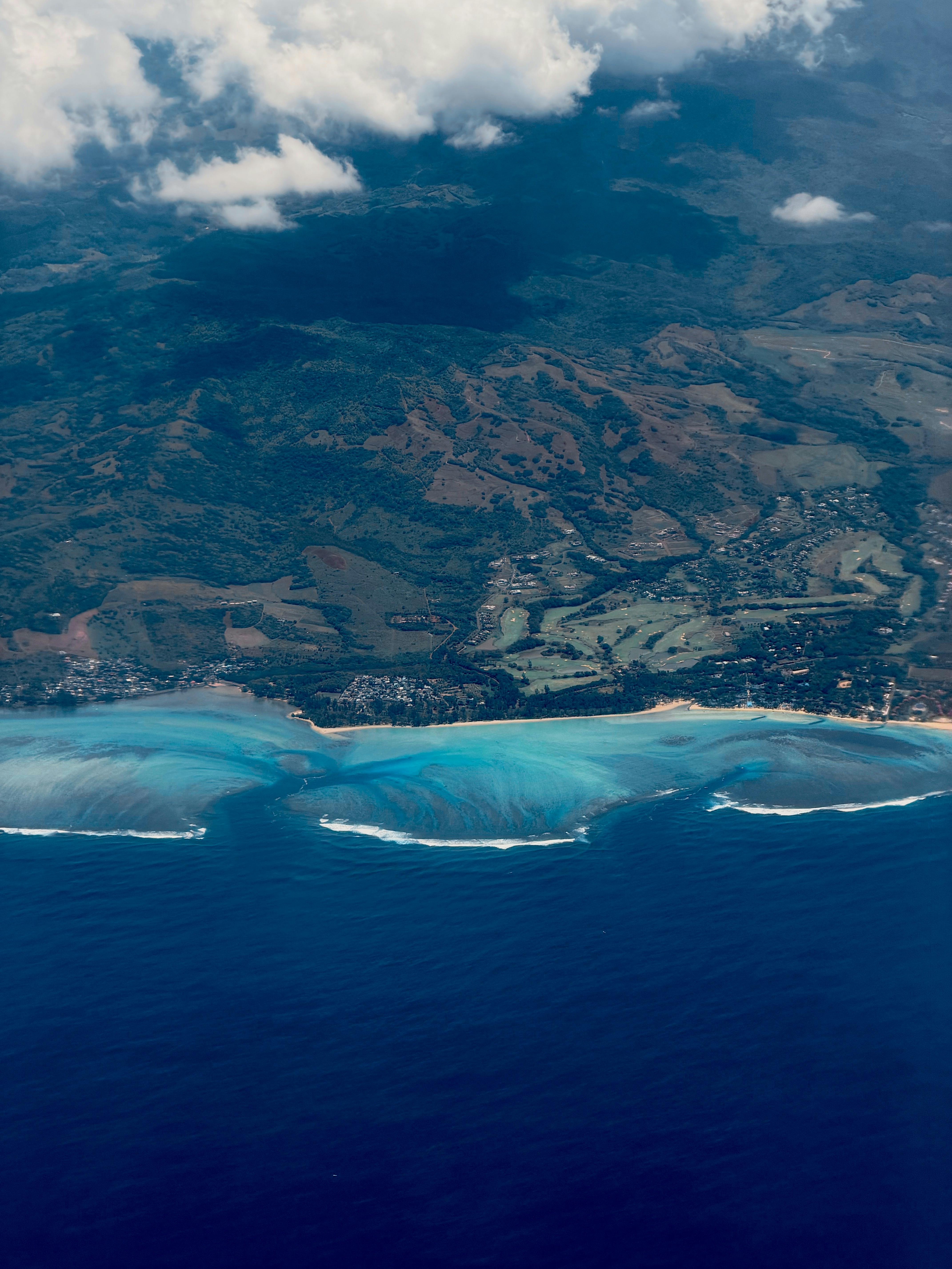 Stunning aerial view of a vibrant coastline and lush landscape beneath scattered clouds.