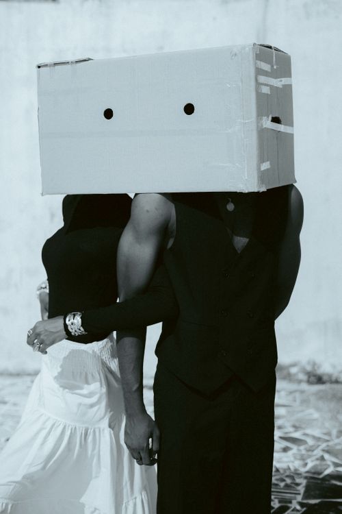 Free Creative image of two people in formal wear with a box covering their heads, creating an artistic and mysterious vibe. Stock Photo