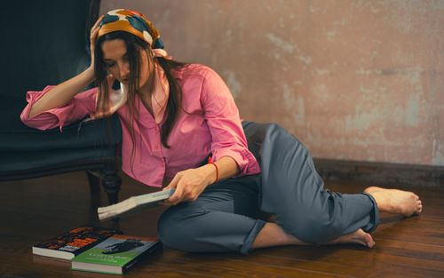 Free Woman in casual attire reading on the floor indoors, expressing relaxation. Stock Photo
