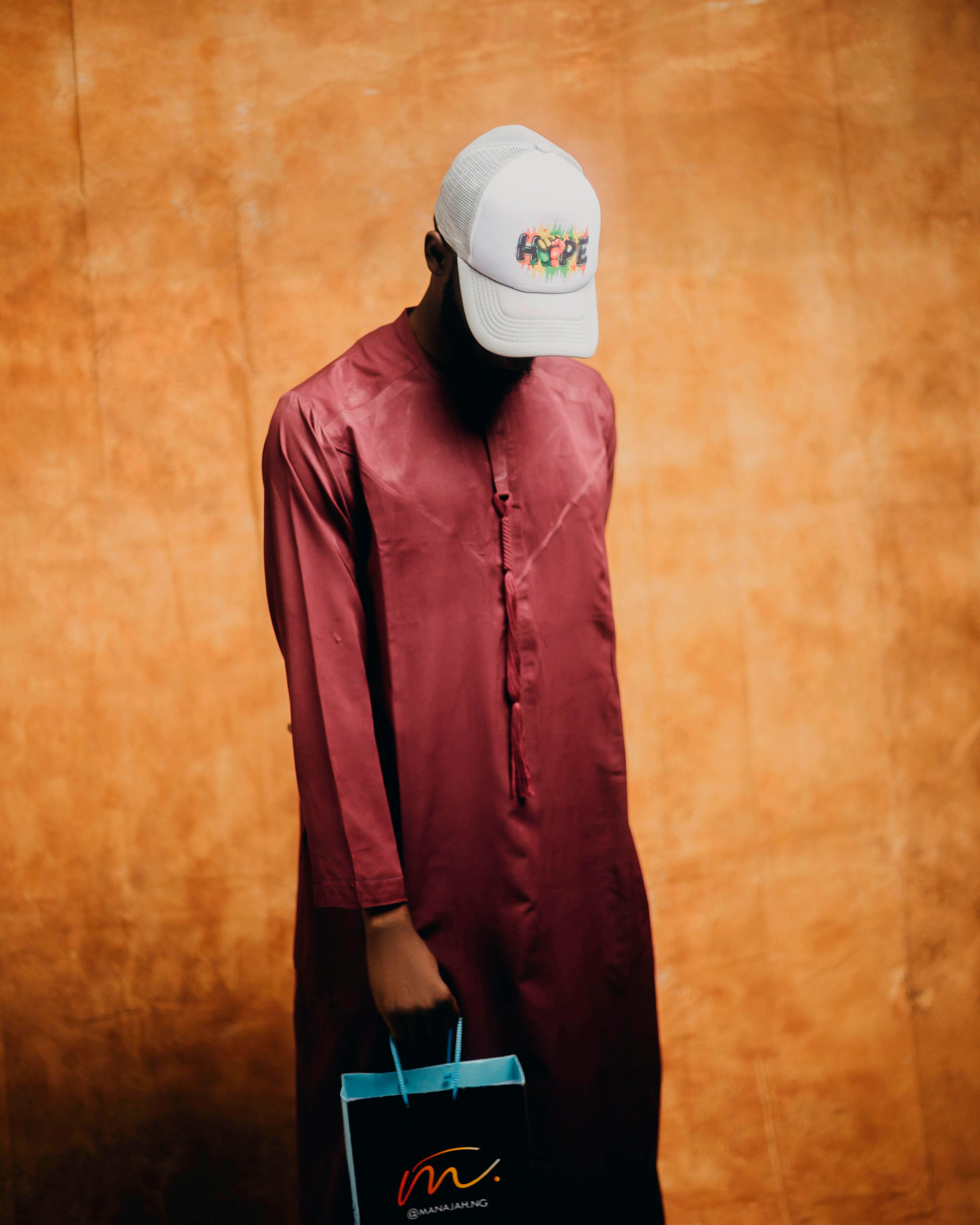 Portrait of a man in traditional attire with a hope cap, holding a gift bag.