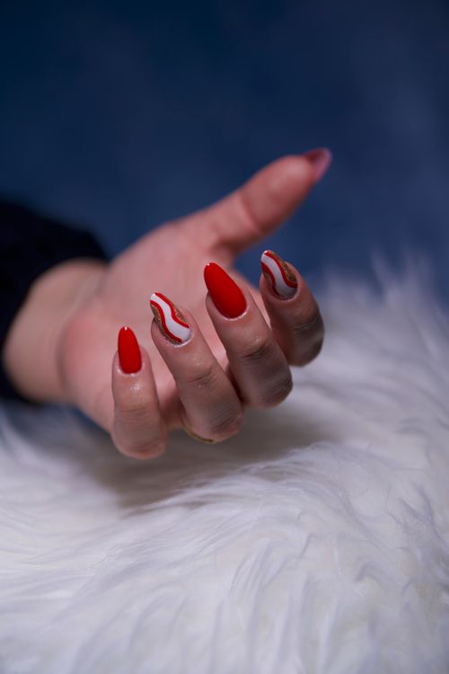 Free Close-up of a hand with artistic red manicure on a white fluffy surface, showcasing unique nail art design. Stock Photo