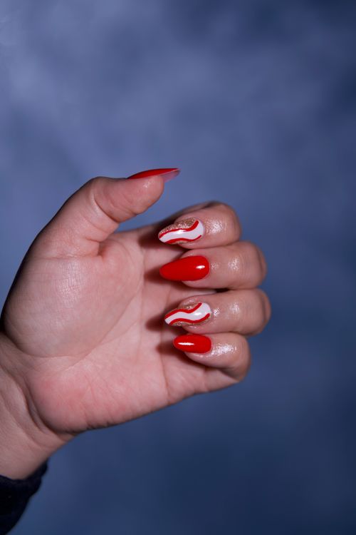 Free Close-up of a hand showcasing stylish red manicured nails with artistic designs. Stock Photo