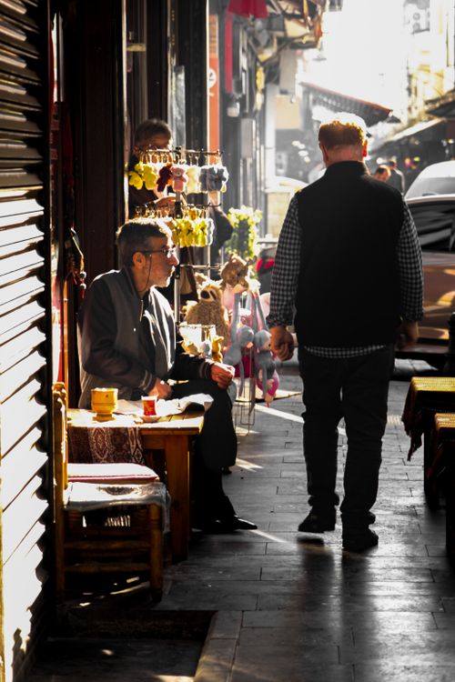 Free Sunlit urban street scene with people enjoying outdoor cafes and shops. Stock Photo