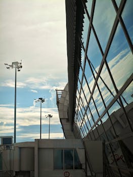 Modern airport terminal with glass facade reflecting a blue sky and clouds.