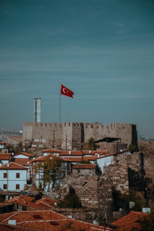 Free View of the ancient Ankara Castle with a Turkish flag flying high, set against a clear sky. Stock Photo