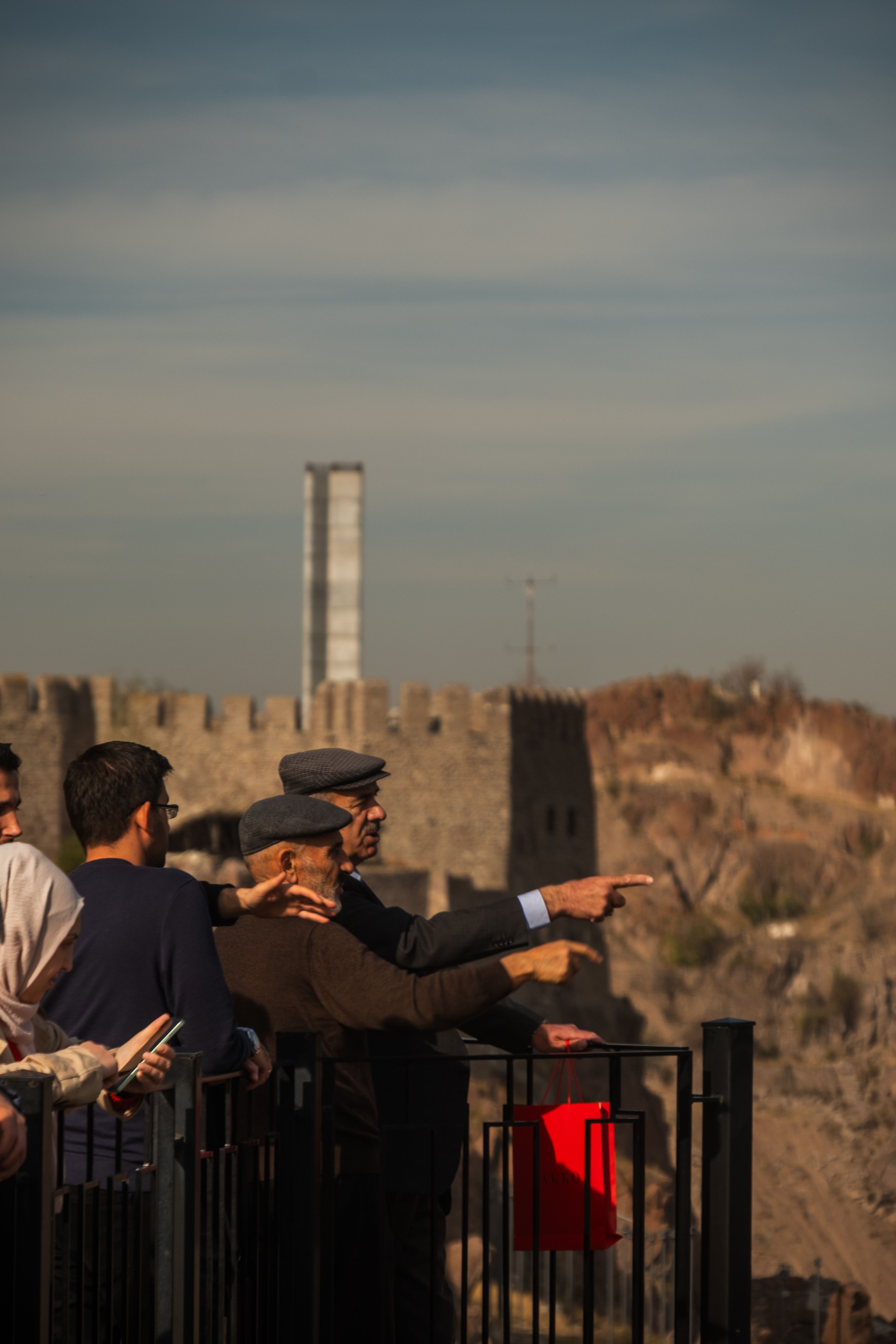 A group of tourists enjoy a scenic view of an ancient castle from an outdoor viewpoint.