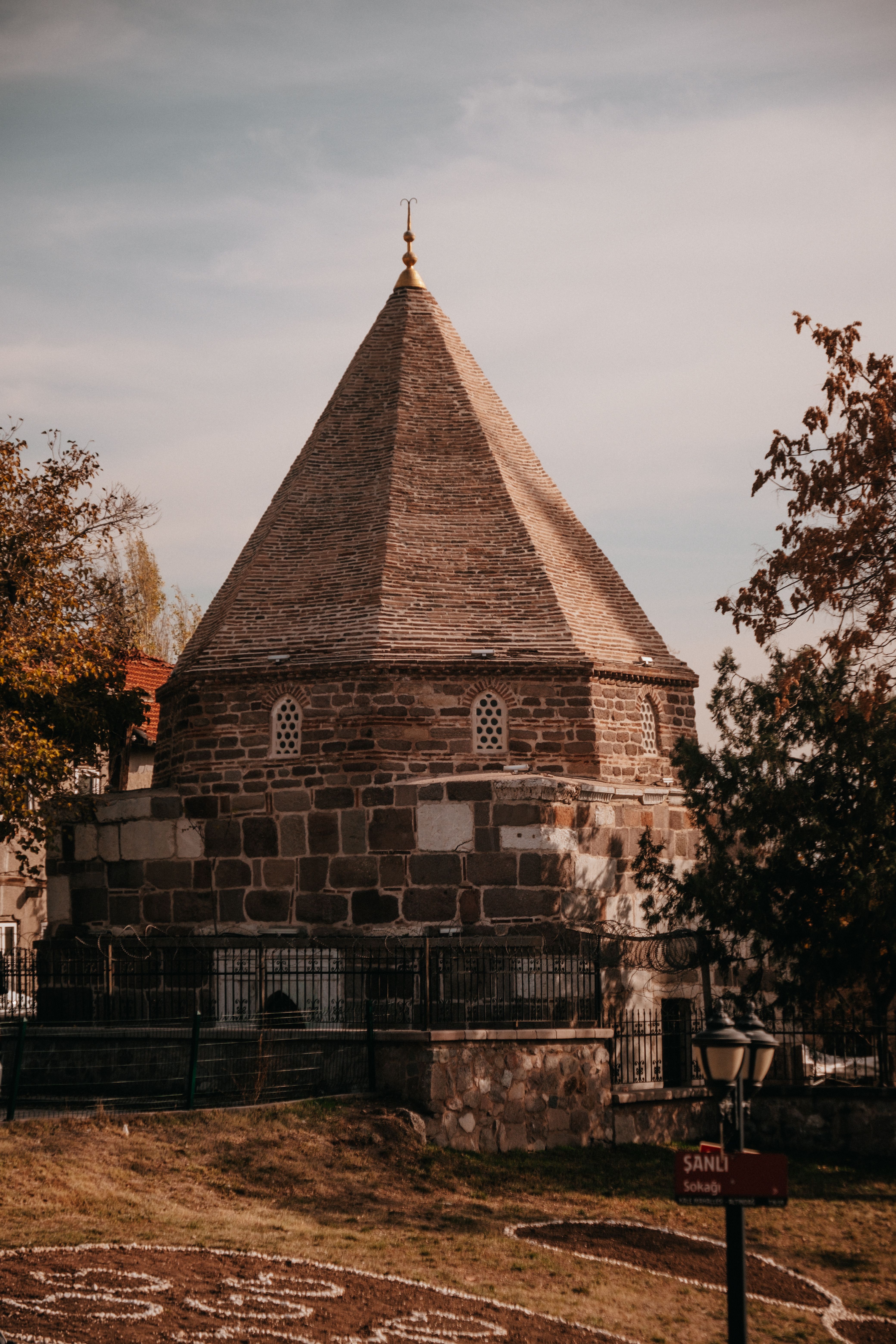 A historic stone building surrounded by autumn trees, featuring a distinctive conical roof.