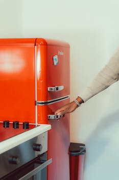 A retro-style red fridge in a modern kitchen with a person's hand on the handle.