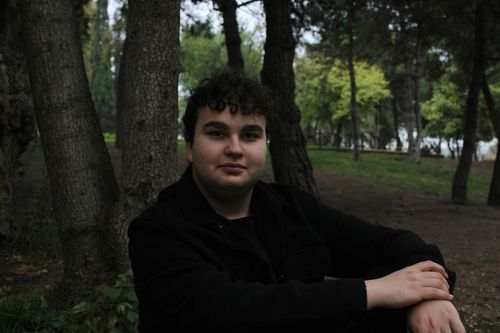 Free Young man sitting in a lush park setting in Darıca, Kocaeli, Türkiye, surrounded by trees. Stock Photo